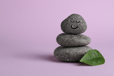 Stack of rocks with drawn smiley face on lilac background, space for text. Harmony and life balanceの写真素材