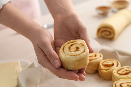 Woman putting cinnamon roll into baking dish at table, closeupの写真素材