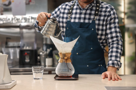 Barista brewing coffee in glass coffeemaker with paper filter at table in cafe, closeupの写真素材