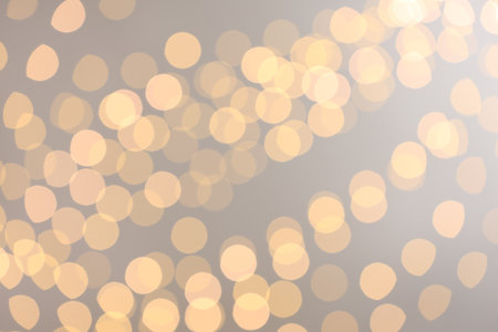 Blurred view of golden lights on light background, bokeh effect