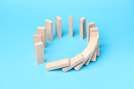 Domino effect. Wooden blocks falling on light blue background