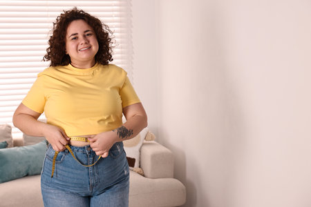 Happy plus size woman measuring waist with tape at home. Space for textの写真素材