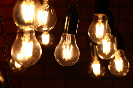 Glowing light bulbs hanging on dark background, closeup