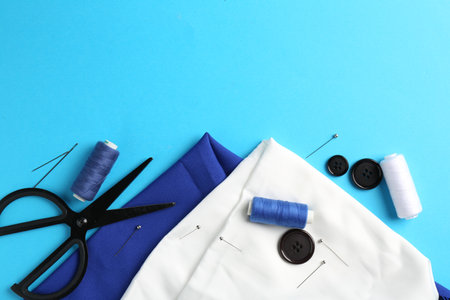 Different sewing supplies on light blue background, flat lay. Space for text