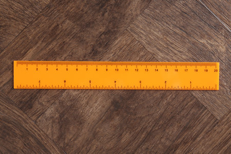 One orange ruler on wooden table, top view
