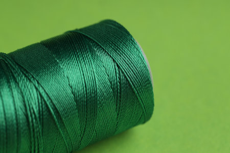Spool of sewing thread on green background, closeup. Space for text