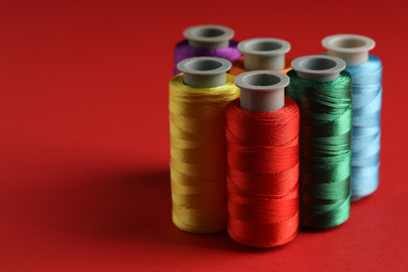 Different spools of sewing threads on red background, closeup. Space for textの写真素材
