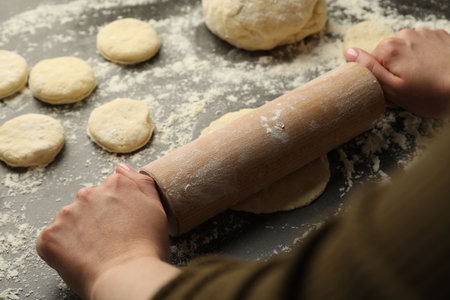 Woman shaping dough with rolling pin at gray table, closeup