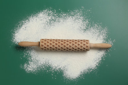 Wooden rolling pin and flour on green background, top view