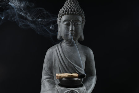 Smoldering palo santo stick and Buddha statue on black background, closeupの写真素材