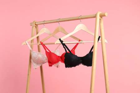 Hangers with beautiful bras on wooden rack against pink backgroundの写真素材