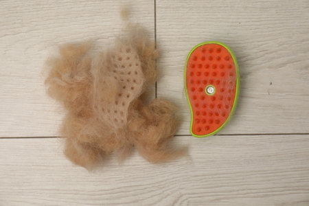 Grooming brush and pile of pet's hair on floor, top view