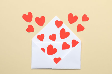 Valentine's Day. Envelope with many paper hearts on beige background, top view