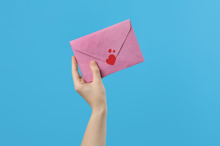 Woman holding pink envelope with red heart stickers on light blue background, closeup. love letterの写真素材