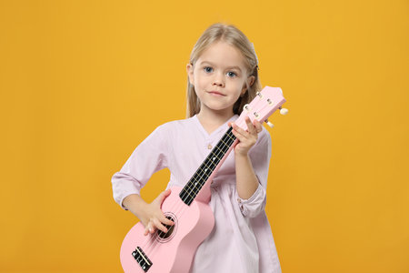 Little girl playing ukulele on orange backgroundの写真素材