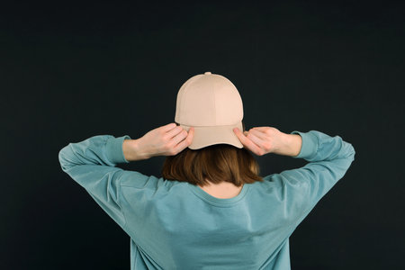 Woman in stylish baseball cap on black background, back view. Mockup for design