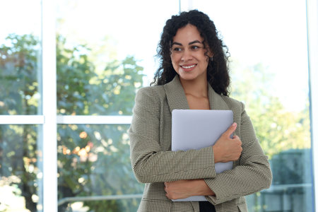 Portrait of young woman with laptop wearing stylish suit indoors