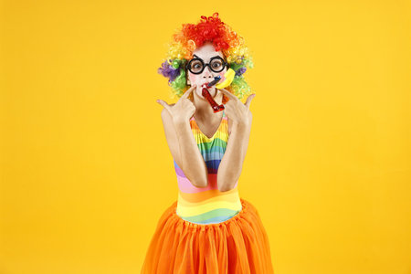 Girl dressed like clown pointing on yellow background. Surprise partyの写真素材
