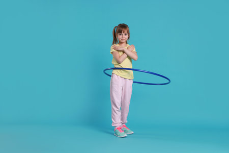 Cute little girl exercising with hula hoop on light blue backgroundの写真素材