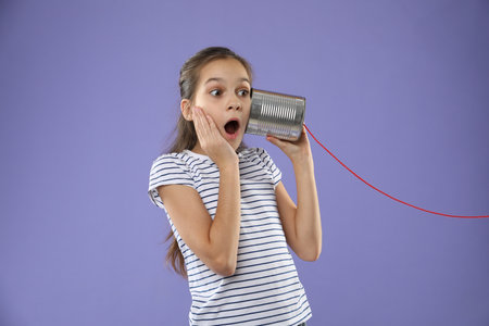 Girl using tin can telephone on violet backgroundの写真素材