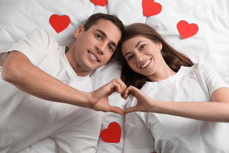 Lovely couple making heart with hands on bed, top view. Valentine's day celebrationの写真素材