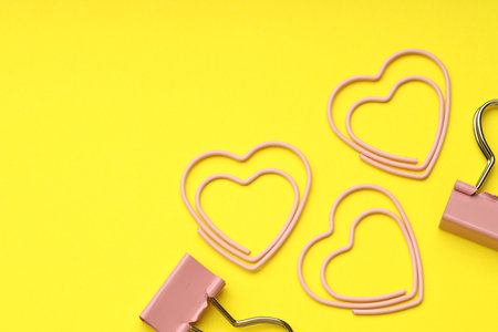 Heart shaped paper and binder clips on yellow background, flat lay. Space for textの写真素材