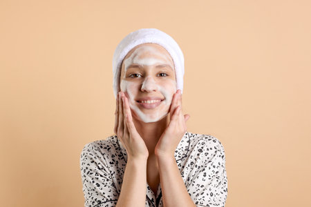 Teenage girl washing her face with cleanser on beige background.の写真素材