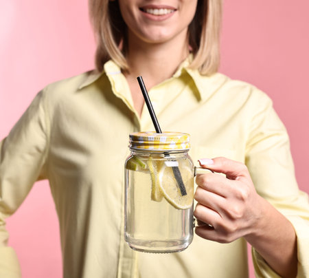 Woman with mason jar of lemonade on pink background, closeup. Refreshing drinkの写真素材