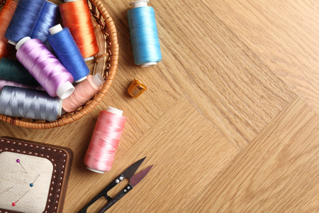 Sewing threads, snips, pincushion and thimble on wooden table, flat lay. Space for text