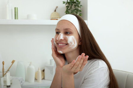 Teenage girl with cleansing foam on her face at home. Acne treatmentの写真素材