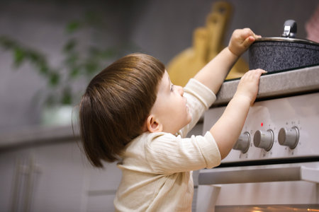 Little boy playing with pot on stove in kitchen. Dangerous situationの写真素材