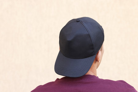 Man in stylish baseball cap near beige wall, back view. Mockup for design