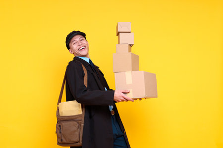 Happy postman with bag and parcels on yellow backgroundの写真素材