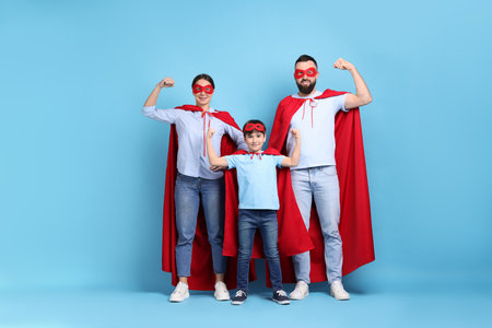 Parents and their son wearing superhero costumes on light blue backgroundの写真素材