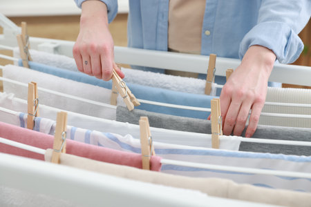 Woman fresh clean laundry on drying hanging rack at home, closeup