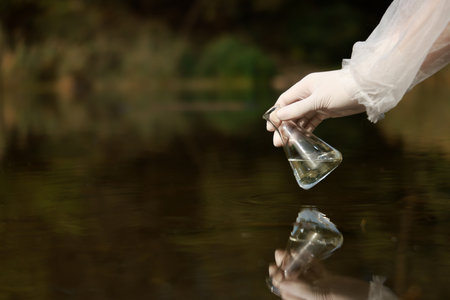 Examination of water quality. Researcher holding flask with sample from lake outdoors, closeup....