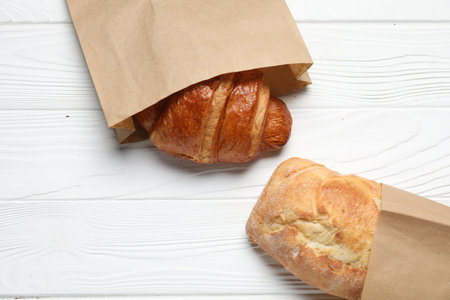 Paper bag with fresh baguette and croissant on white wooden table, top viewの写真素材