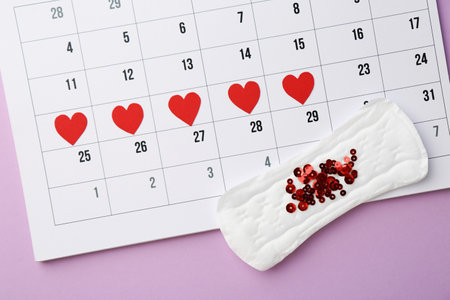 Calendar with marked dates and menstrual pad with sequins on lilac background, top viewの写真素材