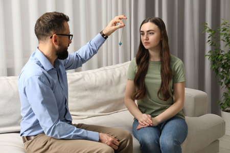 Psychologist using pendulum while working with patient during hypnosis session indoors