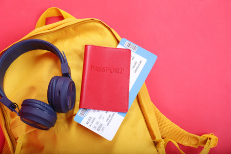 Backpack, headphones and passport with ticket on red background, closeup. Travel abroad