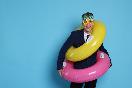 Businessman with inflatable rings and funny sunglasses on light blue background, space for text