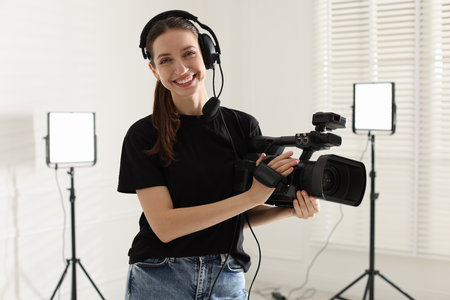 Happy woman with professional video camera and headset in studio