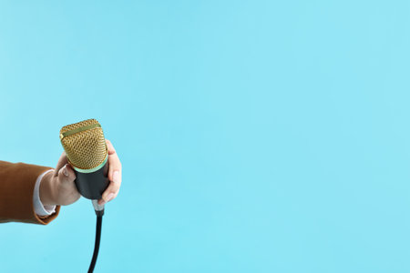 Woman with microphone on light blue background, closeup. Space for textの写真素材