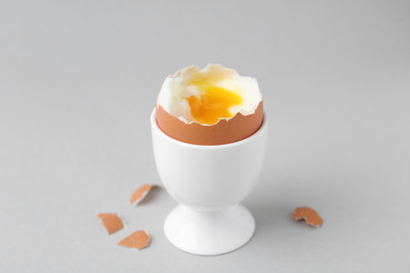 Soft boiled egg in cup and eggshell on light gray backgroundの写真素材