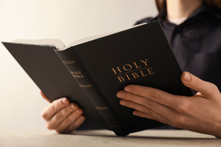 Woman reading Holy Bible at beige table, closeup