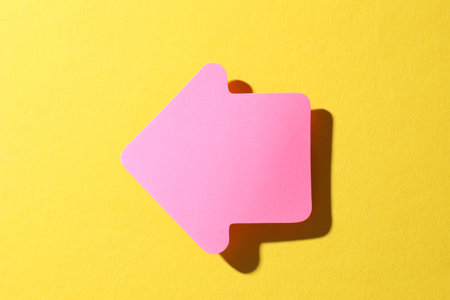 One pink paper arrow on yellow background, top viewの写真素材