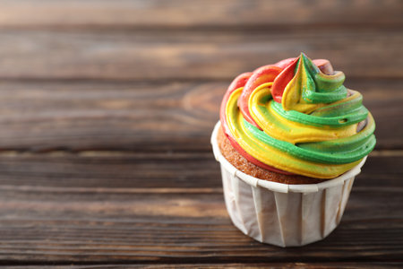 Delicious cupcake with colorful cream on wooden table, closeup. Space for textの写真素材
