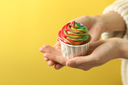 Woman holding delicious cupcake with colorful cream on yellow background, closeup. Space for textの写真素材