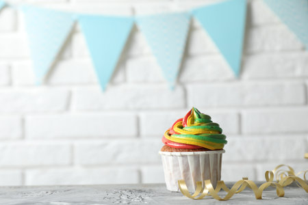 Delicious cupcake with colorful cream on gray textured table near white brick wall. Space for textの写真素材