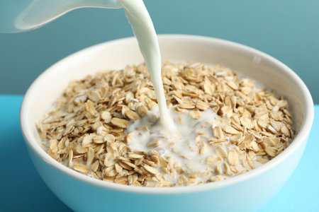 Pouring milk into bowl with oatmeal at light blue table, closeupの写真素材